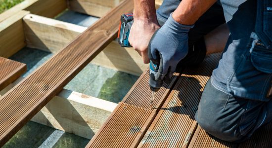 Deck construction, builder hand with electric screwdriver installing impregnated wooden boards