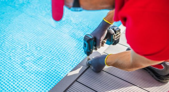 Poolside Composite Deck Building by Professional Worker. Modern Swimming Pool Surrounding. Using Cordless Drill Driver.