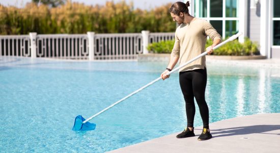 Young man professional cleaner worker cleaning pool with scoop net outdoors.
